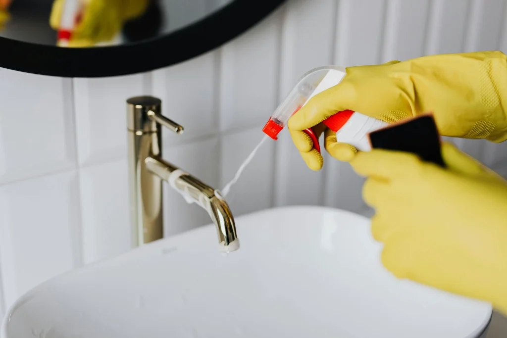 Profissional de housekeeping usando luvas amarelas e borrifador para limpeza doméstica profissional em Salvador.